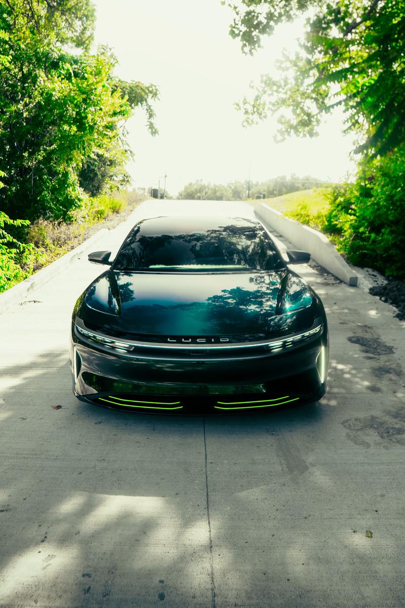 Green sedan with colored paint protection film on a tree lined road